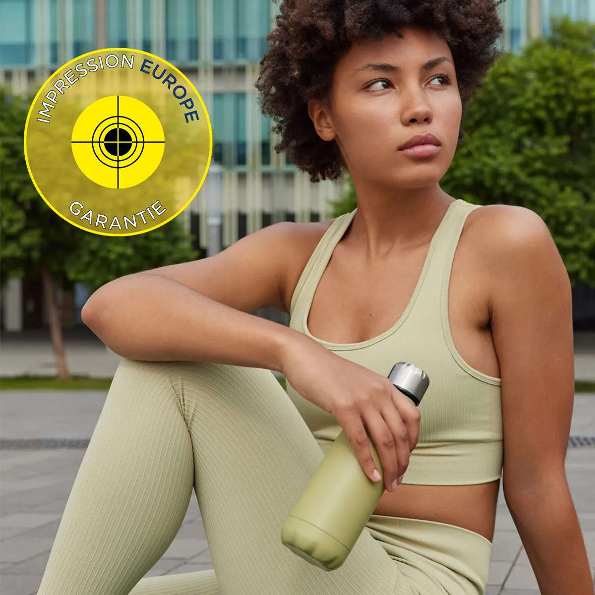 objets-et-gourdes-impression-europe-garantie Femme sportive en tenue beige tenant une gourde assortie, avec le logo 'Impression Europe Garantie' en arri